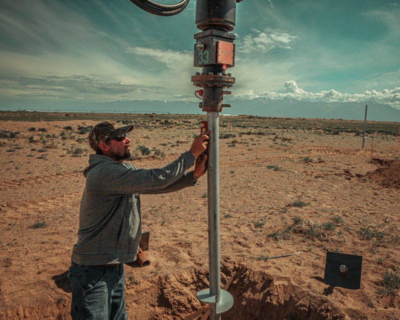 Installer holding a helical pier plumb as the drive head turns it into the ground