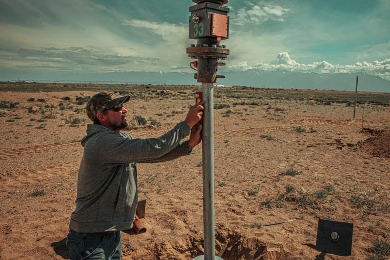Site Safe installer holding a helical pier shaft plumb on an open building lot