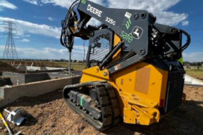 Tracked loader with a pier drive attachment beside new foundation walls on a residential lot