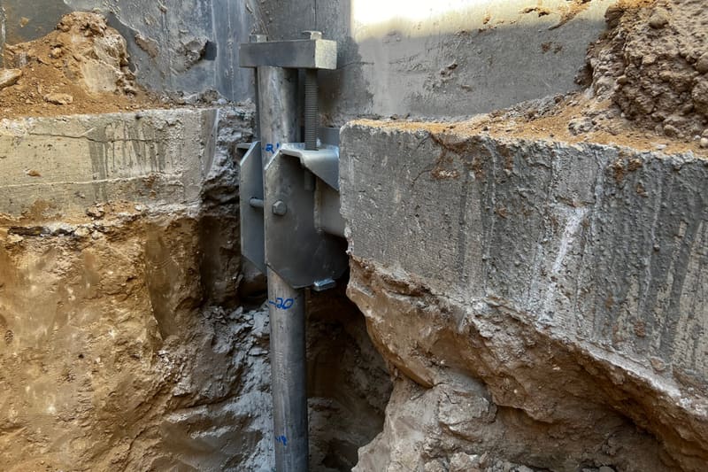 Helical pier bracket against a foundation wall, with the soil layers exposed