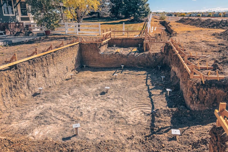 Excavated backyard pool site with pier markers set across its floor