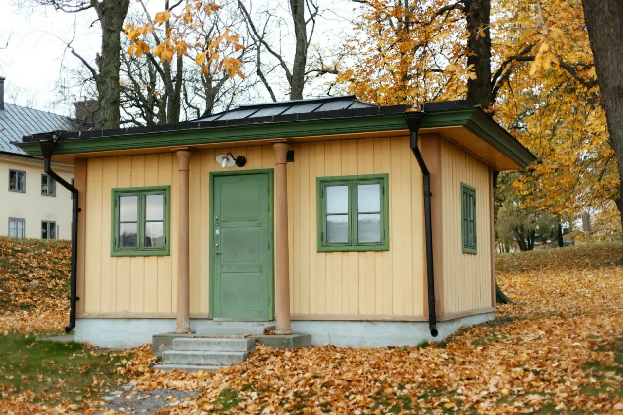 Small detached one-story wooden building with a green door and porch posts, the size of a typical backyard ADU