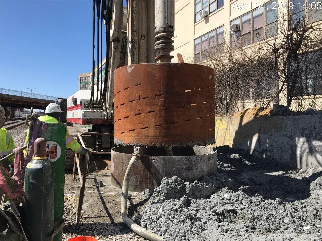 Drill rig with a steel casing over a drilled shaft, the hole for a caisson foundation, with auger spoils piled beside it