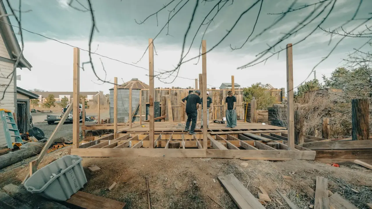 Deck framing going up on posts in a backyard, the stage where footings or helical piles carry the load