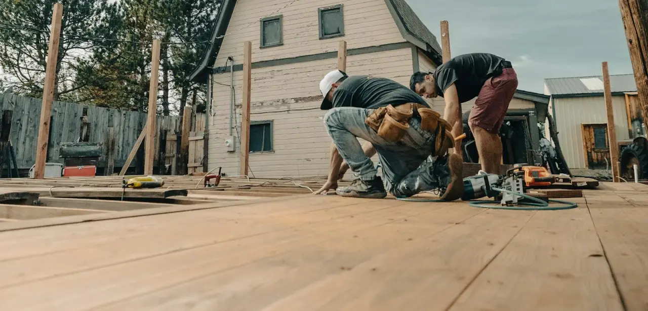Two carpenters fastening decking on a new wood deck with support posts standing along the edge