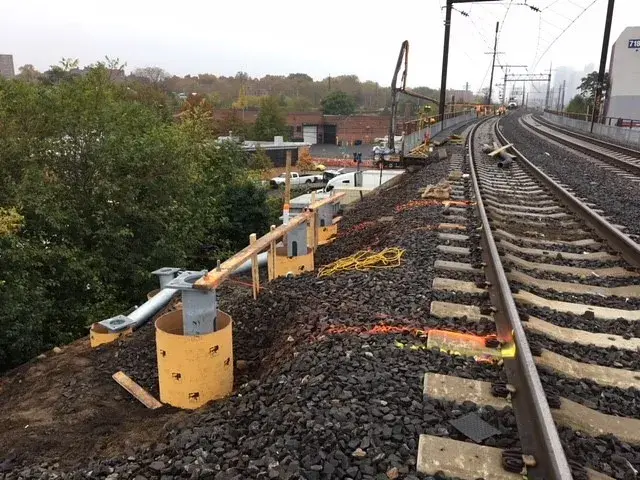 Helical pier foundation system tops with steel cap plates set inside round forms, ready for concrete pile caps beside a rail line