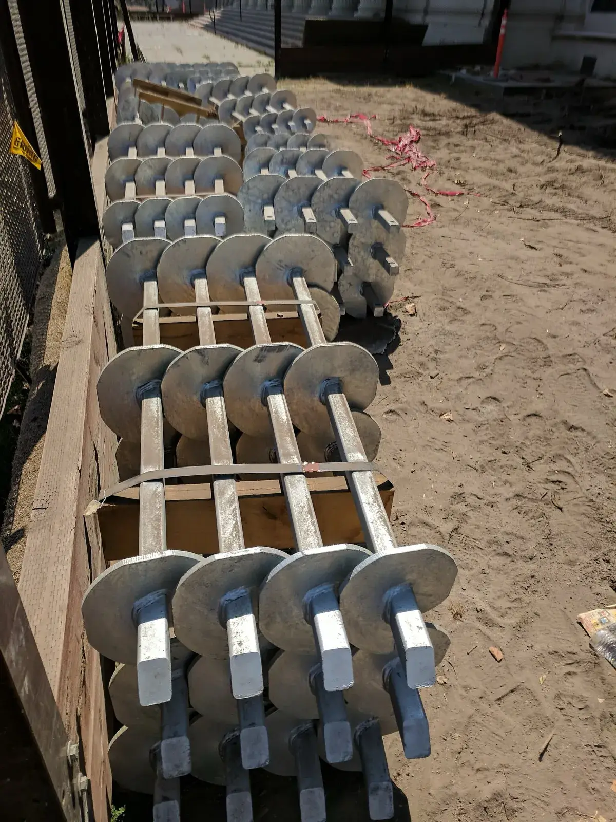 Galvanized square-shaft helical piles for new construction stacked on pallets at a school jobsite