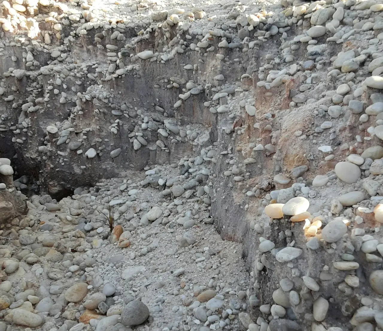 Excavated trench with walls of packed rounded cobbles and gravel