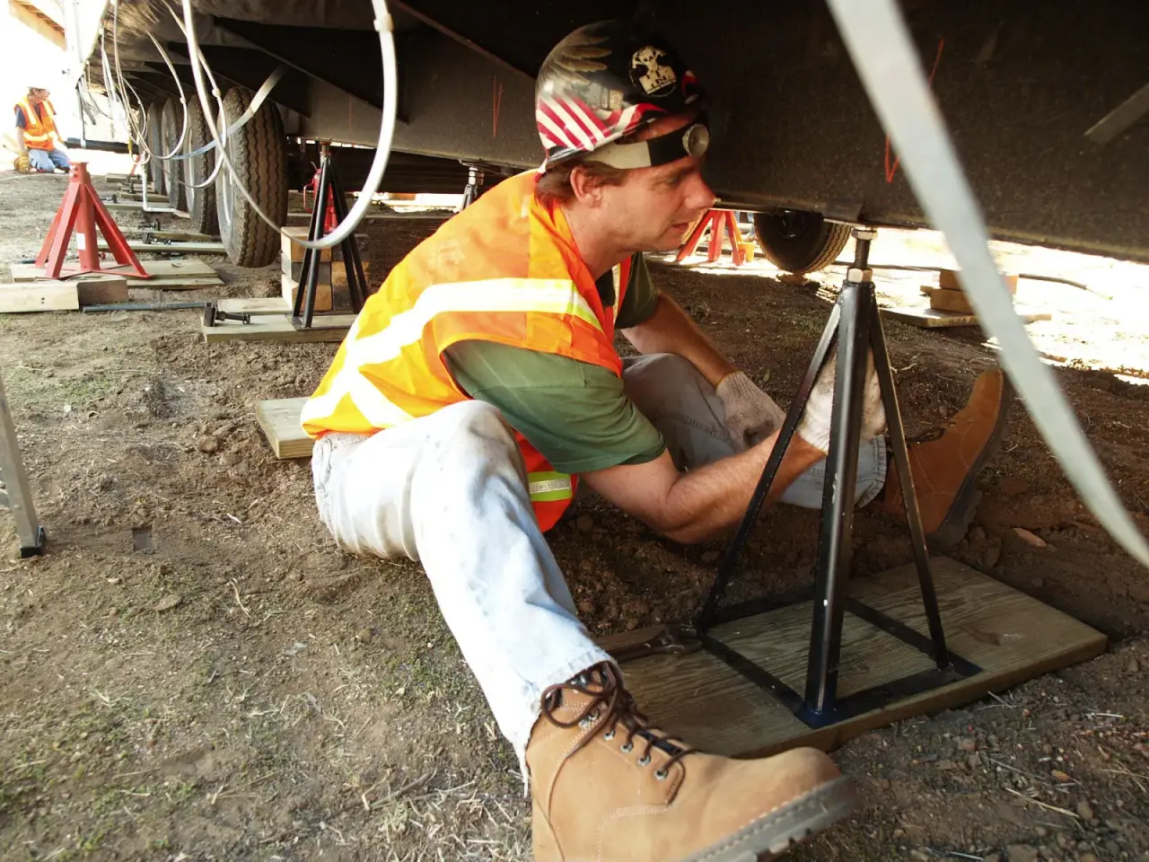 Installer setting adjustable steel pier stands on wood pads under the steel frame of a manufactured home during a new installation