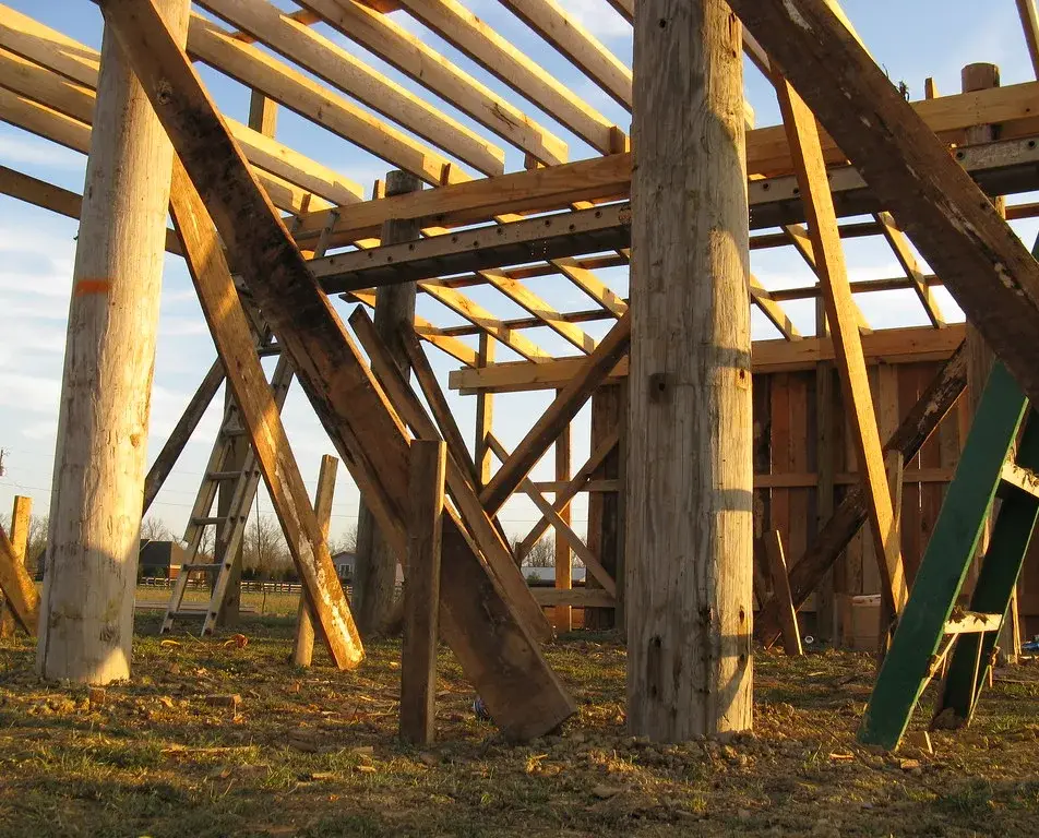 Round wood poles set directly in the ground with temporary diagonal bracing under the roof framing of a pole barn