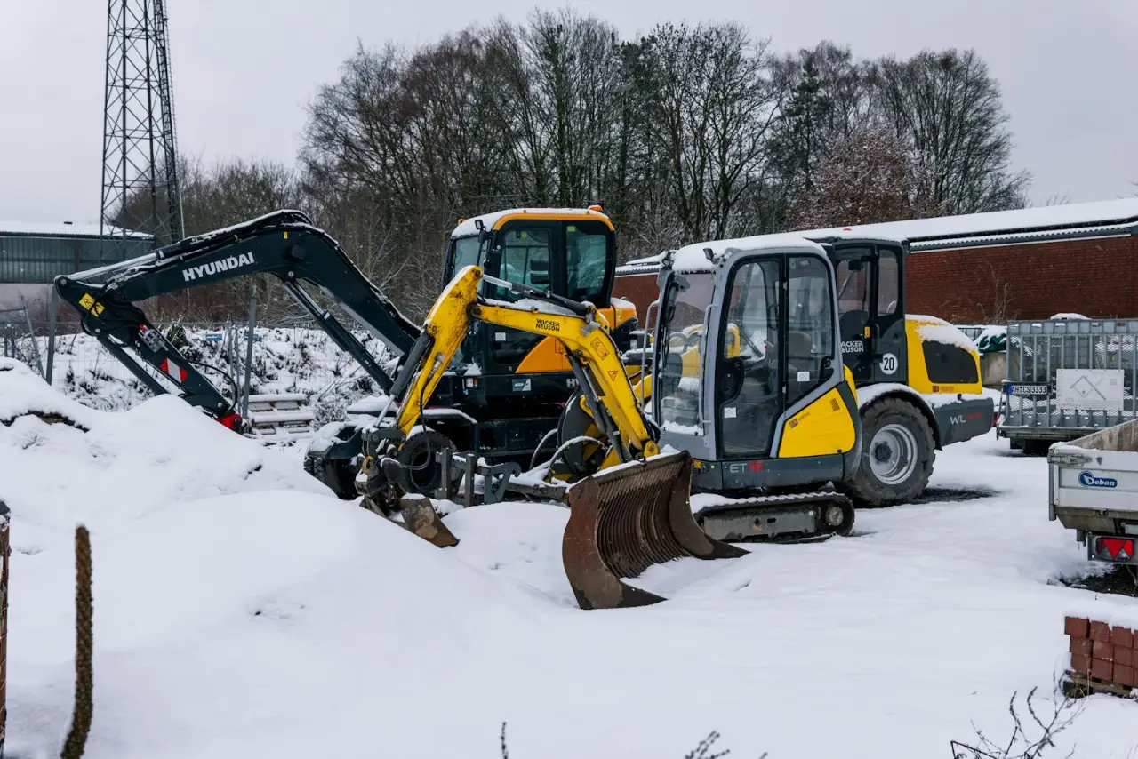 Compact excavators parked on a snowy job site, the size of machine used to install helical piles in winter